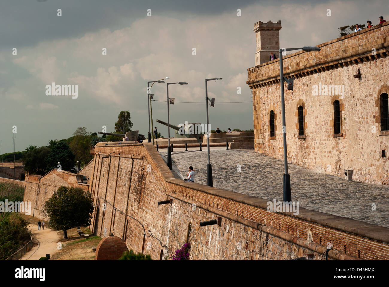 Young couple looks over wall toward sea, World War II guns in background.Castell de Montju Stock Photo