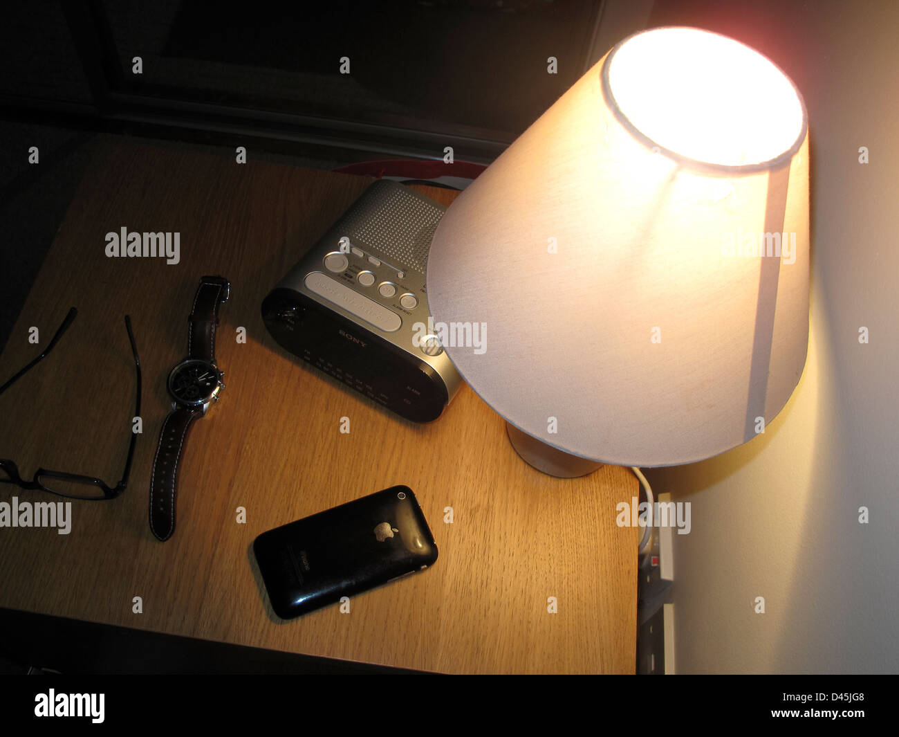Bedside table with lamp clock radio glasses and iPhone Stock Photo