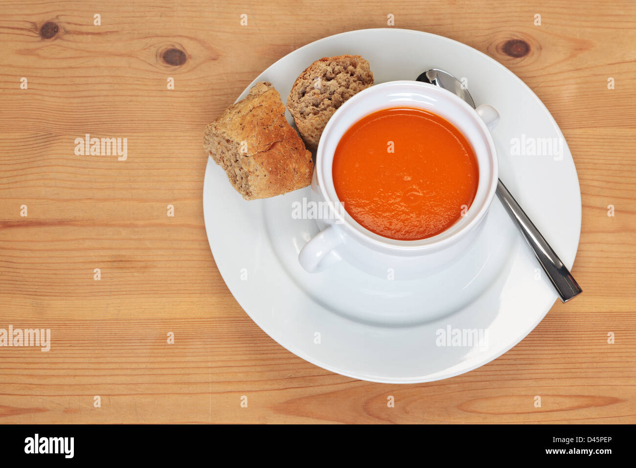 Bowl of hot tomatoe soup with fresh brown granary bread on a wooden table. Stock Photo