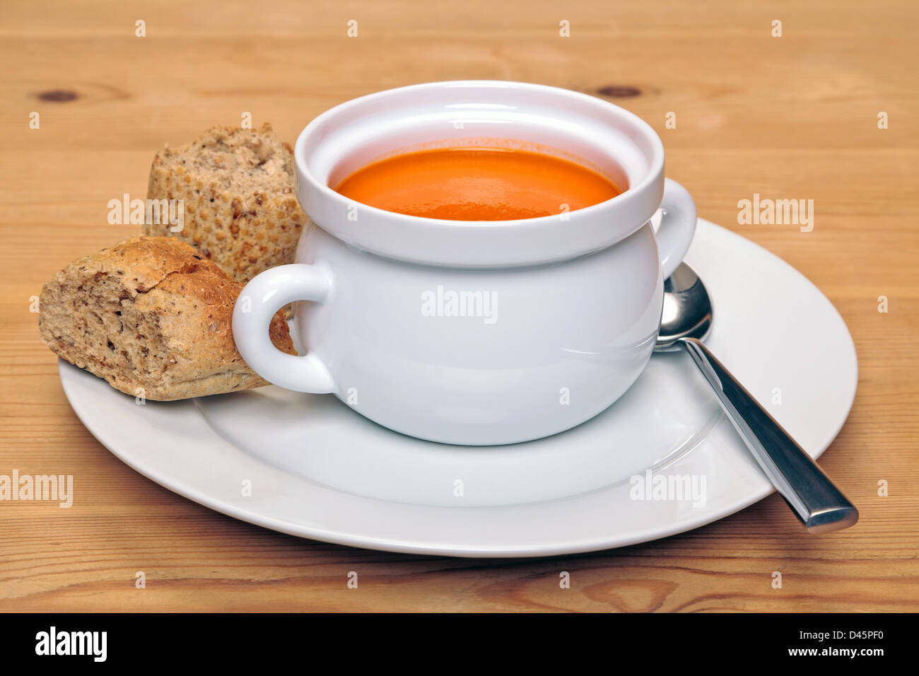 Bowl of hot tomatoe soup with fresh brown granary bread on a wooden table. Stock Photo