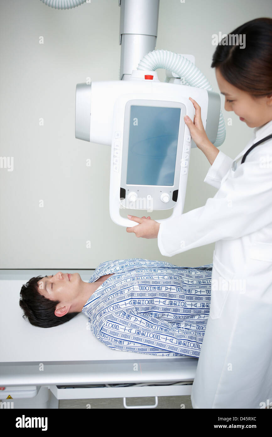 a patient lying on a bed and a doctor using x ray machine Stock Photo