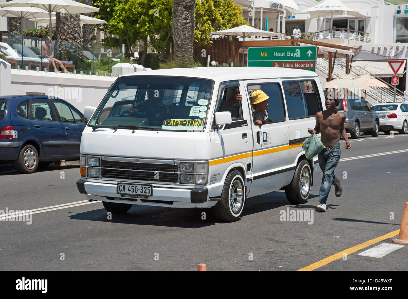Man carrying plastic bag running for a 'black' taxi in Camps Bay Western Cape South Africa Stock Photo