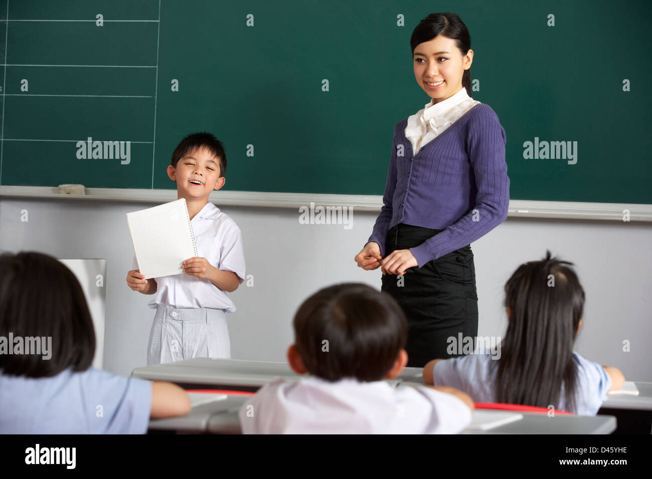 Pupil And Teacher Standing By Blackboard In Chinese School Classroom Stock Photo