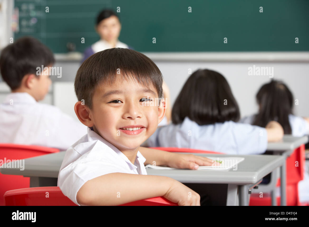 Portrait Of Male Pupil Working At Desk In Chinese School Classroom ...