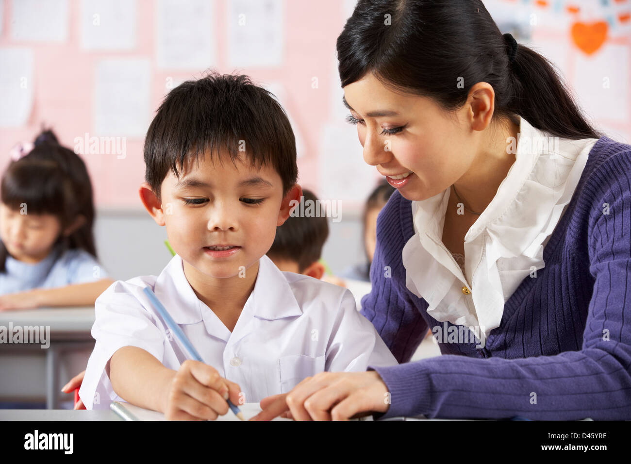Teacher Helping Student Working At Desk In Chinese School Classroom Stock Photo Alamy
