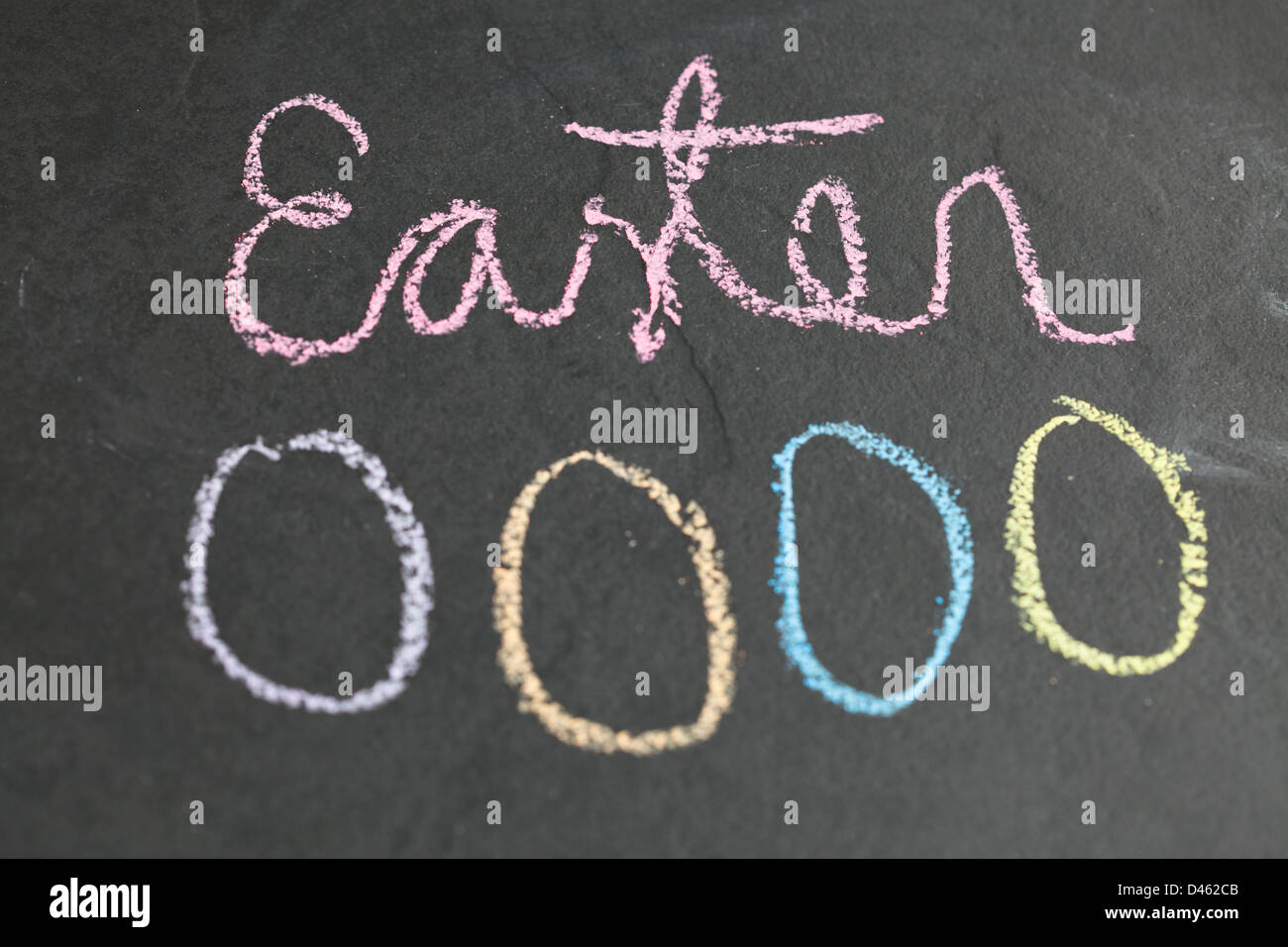 Closeup of four Easter egg shaped chalk drawings and text on dark background Stock Photo