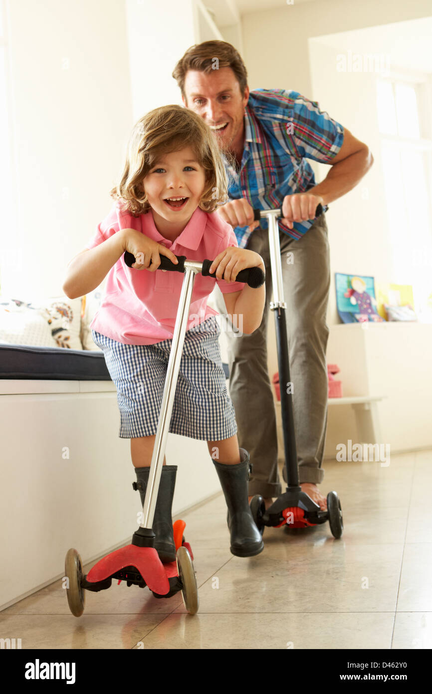 Father And Son Riding Scooters Indoors Stock Photo
