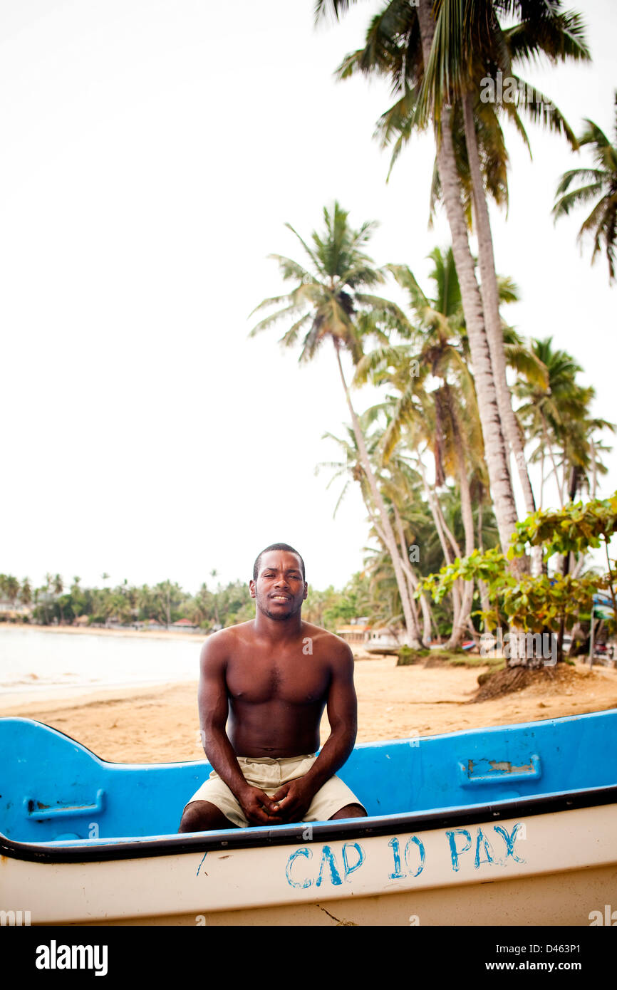 A young man sits in his boat on a sunny day on a beach. Stock Photo