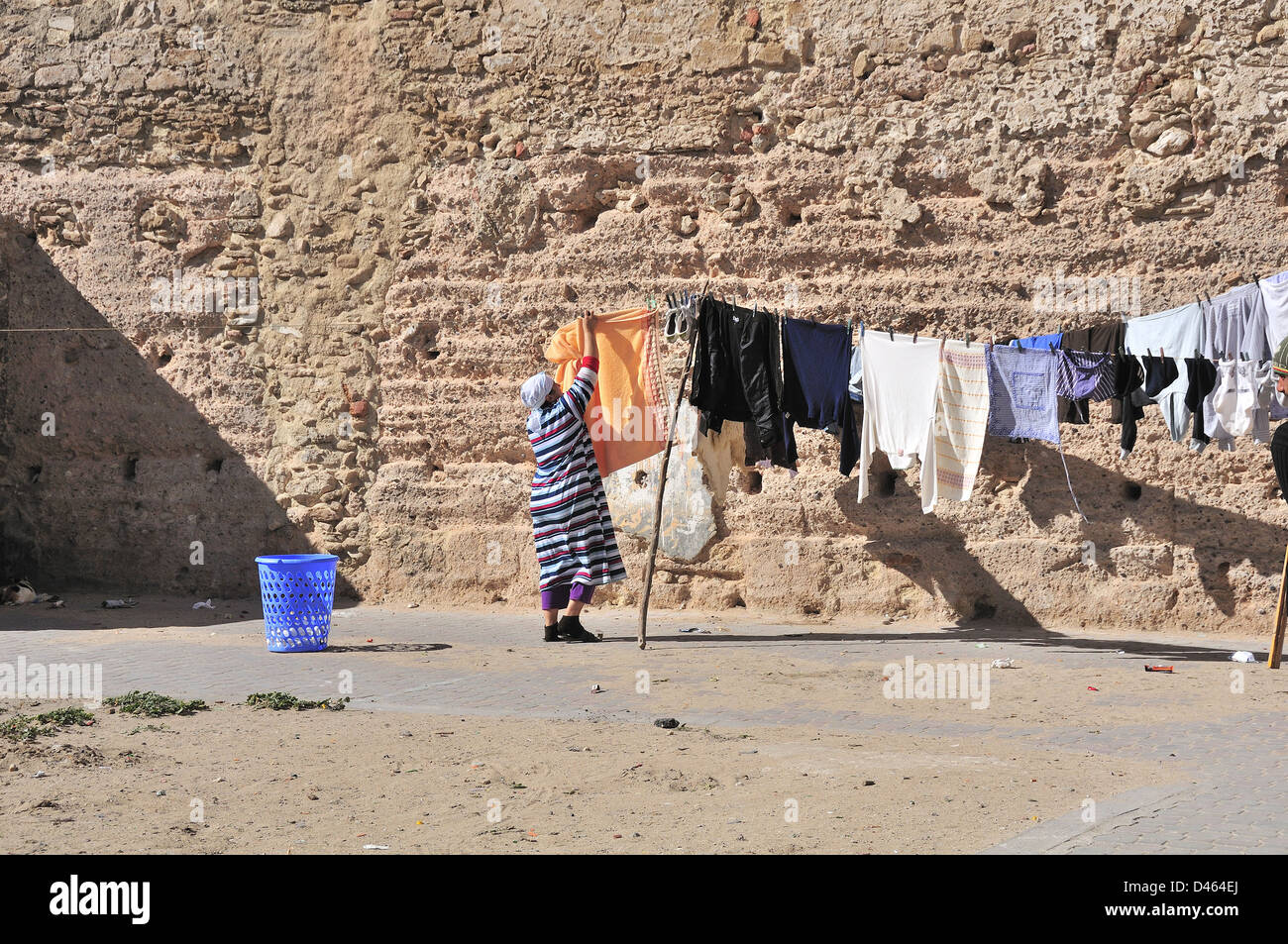Woman in Essaouira, Morocco, hanging her washing outside to dry on line behind high brick wall with the sea beyond Stock Photo
