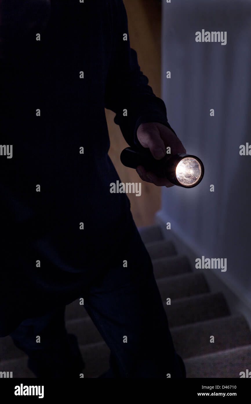 Shadowy male intruder holding a torch or flashlight walking upstairs. Stock Photo