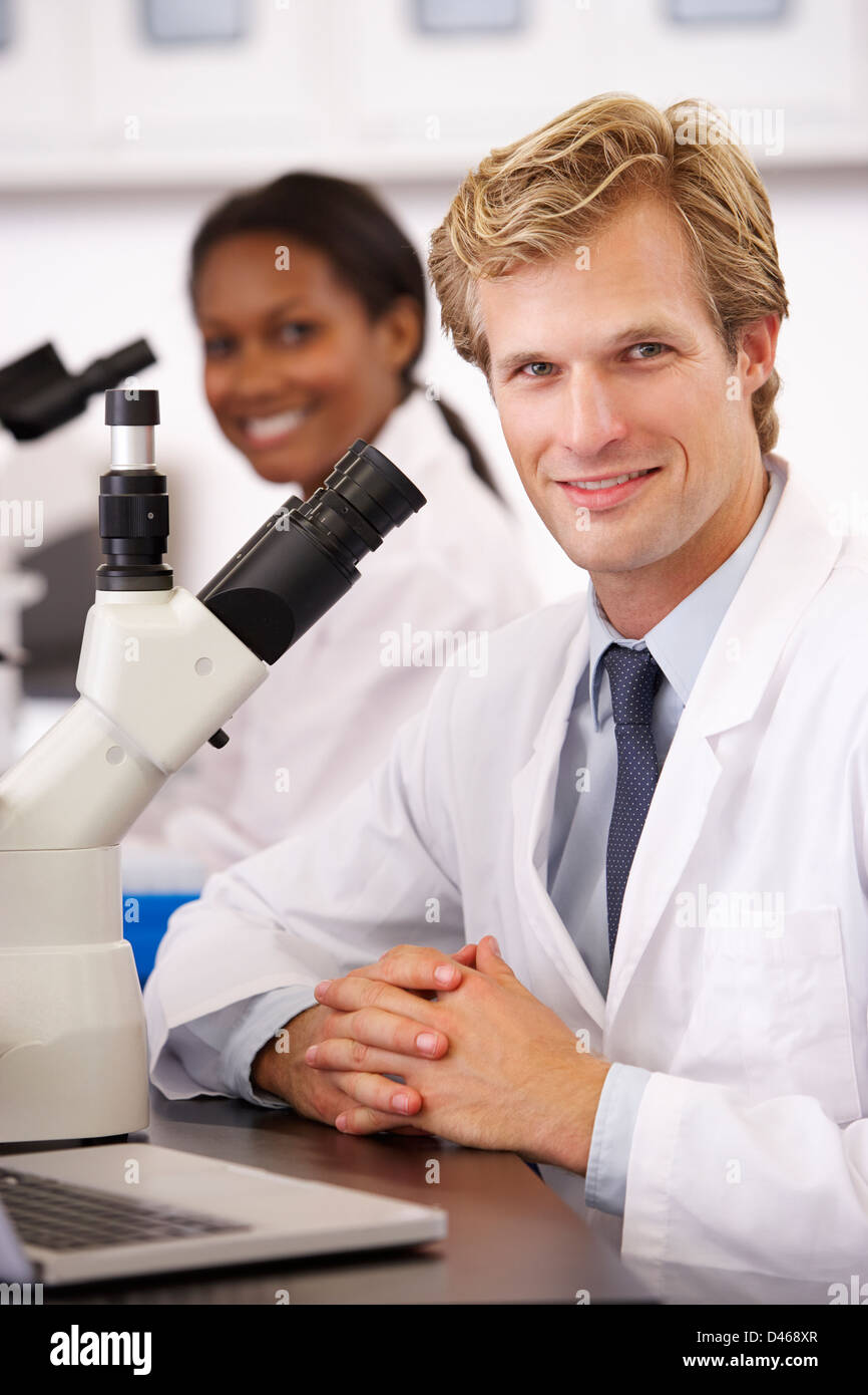 Male And Female Scientists Using Microscopes In Laboratory Stock Photo