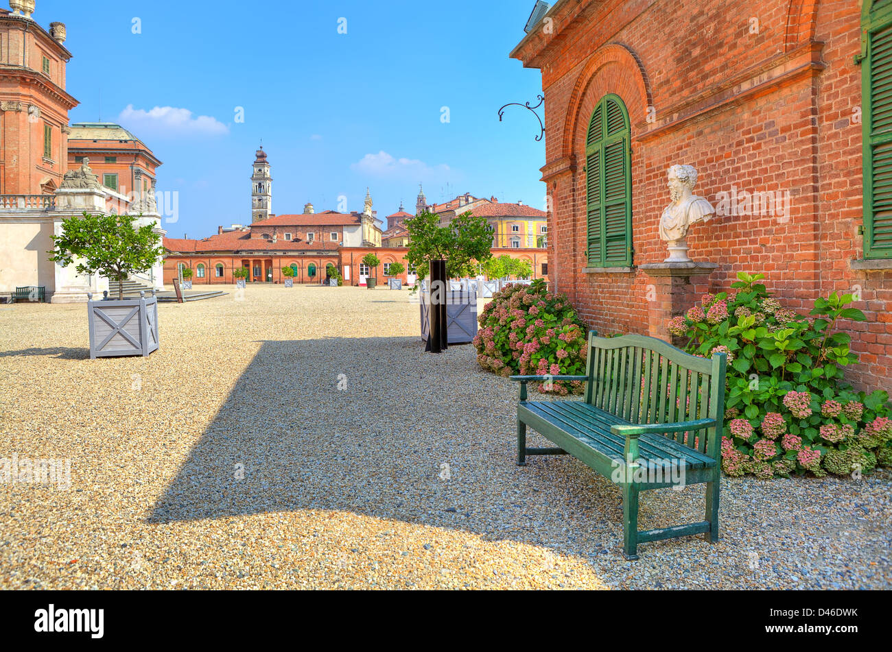 Wooden bench on the gravel next to red brick house at the entrance to park and Royal Castle of Racconigi in Piedmont, Italy. Stock Photo