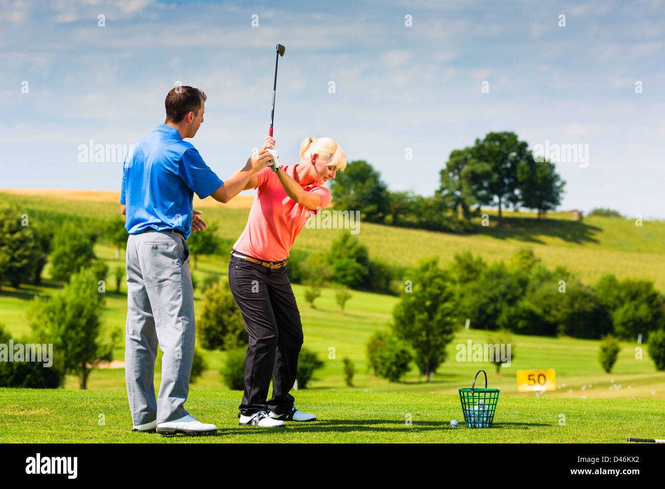 Young female golf player at Driving Range with a Golf Pro, she presumably does exercise Stock Photo