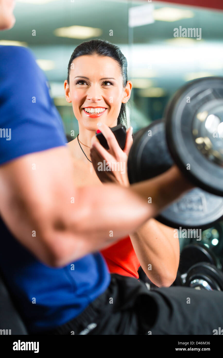 Man or Bodybuilder with his personal fitness trainer in the gym exercising sport with dumbbells, closeup Stock Photo