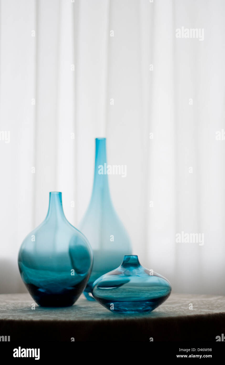 Three Blue Glass Vases Sit On A Table In Front Of A Large Window