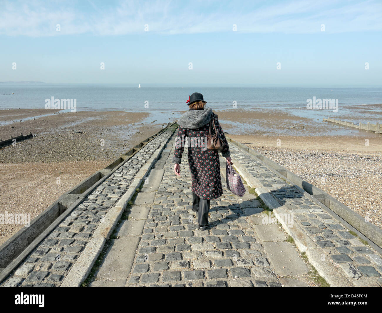 Lady walks down a jetty towards the sea Stock Photo