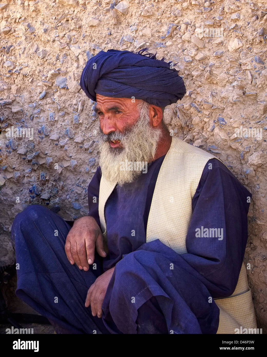 Kandahar, Afghanistan - May 14, 2010: An Afghan village elder takes a rest along a wall after meeting with ISAF Forces. Stock Photo