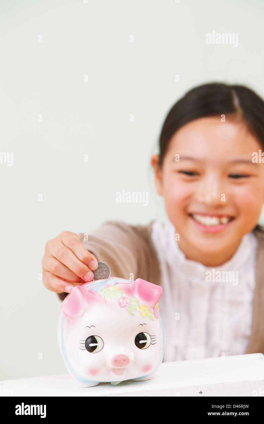 Girl Putting a Coin Into a Piggy Bank Stock Photo - Alamy