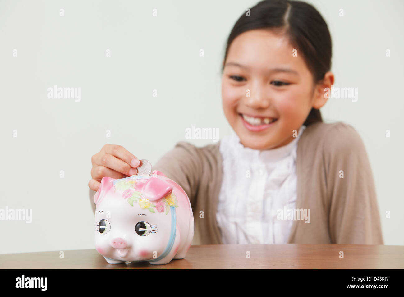 Girl Putting a Coin Into a Piggy Bank Stock Photo - Alamy