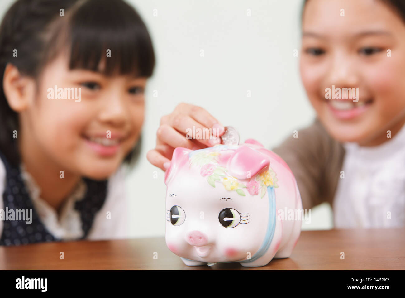 Girls Putting a Coin Into a Piggy Bank Stock Photo - Alamy
