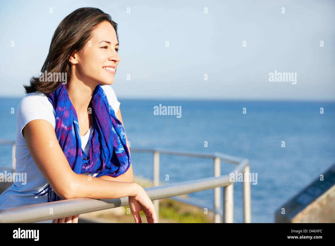 Hispanic Woman Looking Over Railing At Sea Stock Photo