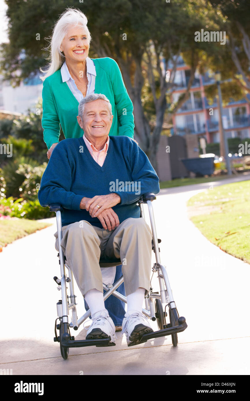 Senior Woman Pushing Husband In Wheelchair Stock Photo