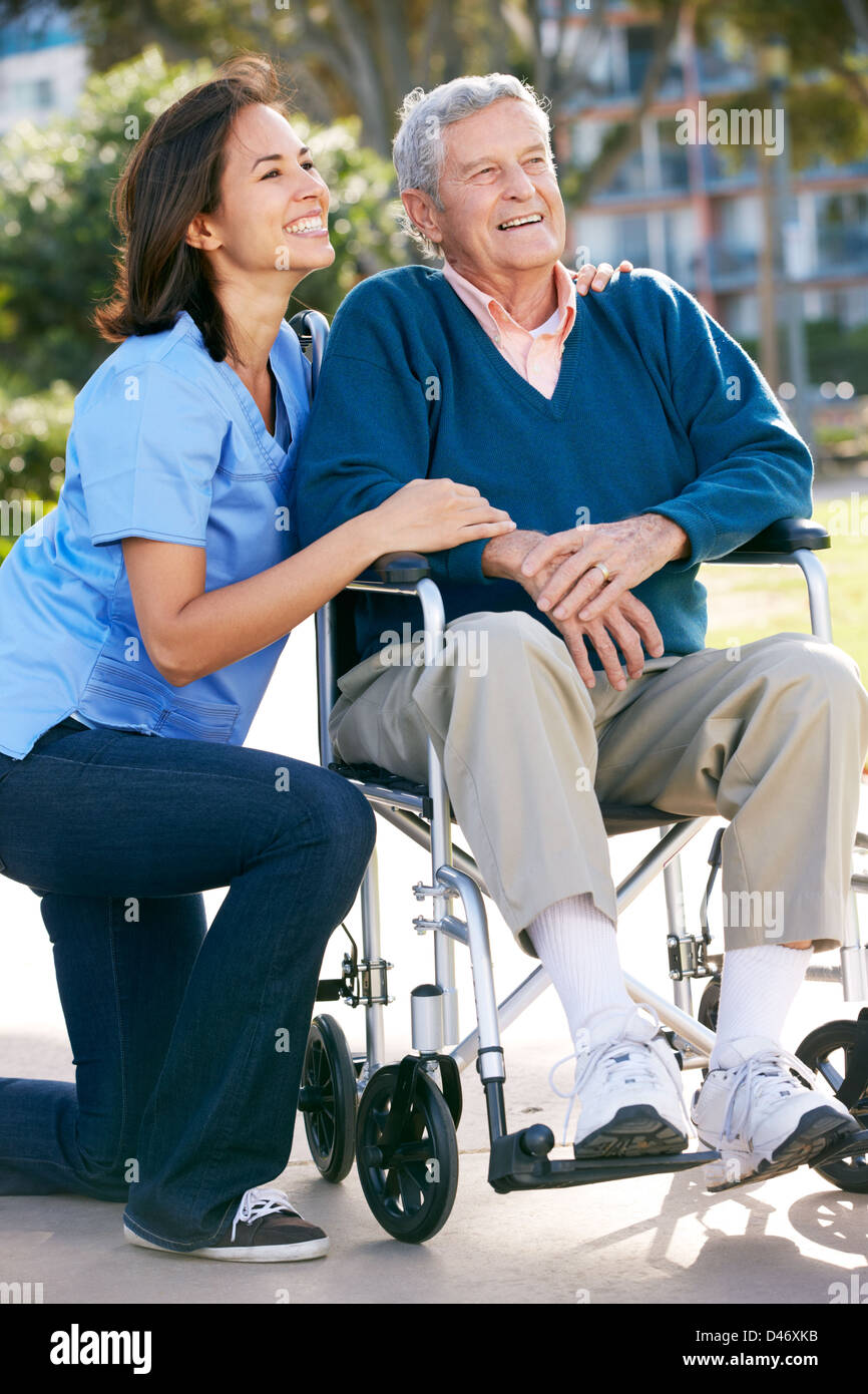 Carer Pushing Senior Man In Wheelchair Stock Photo