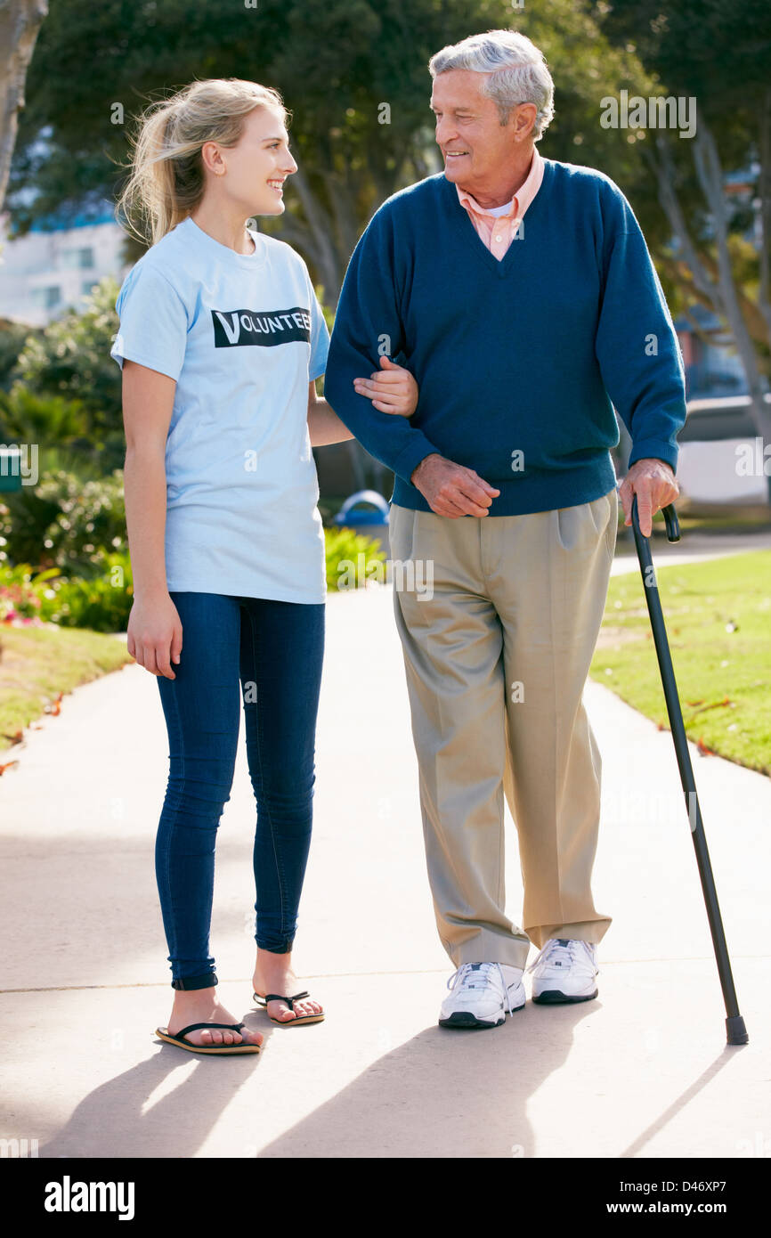 Teenage Volunteer Helping Senior Man Walking Through Park Stock Photo