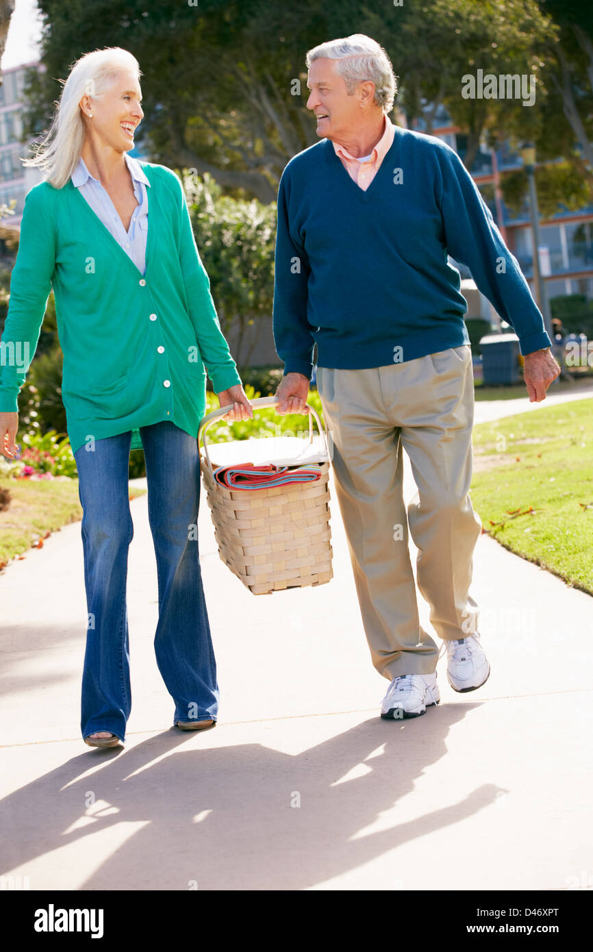 Senior Couple Walking In Park Together With Picnic Basket Stock Photo