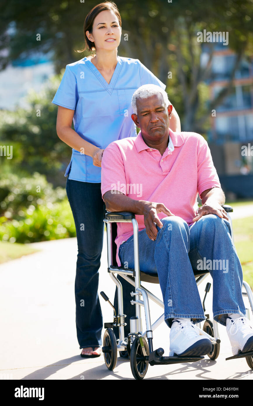 Carer Pushing Unhappy Senior Man In Wheelchair Stock Photo