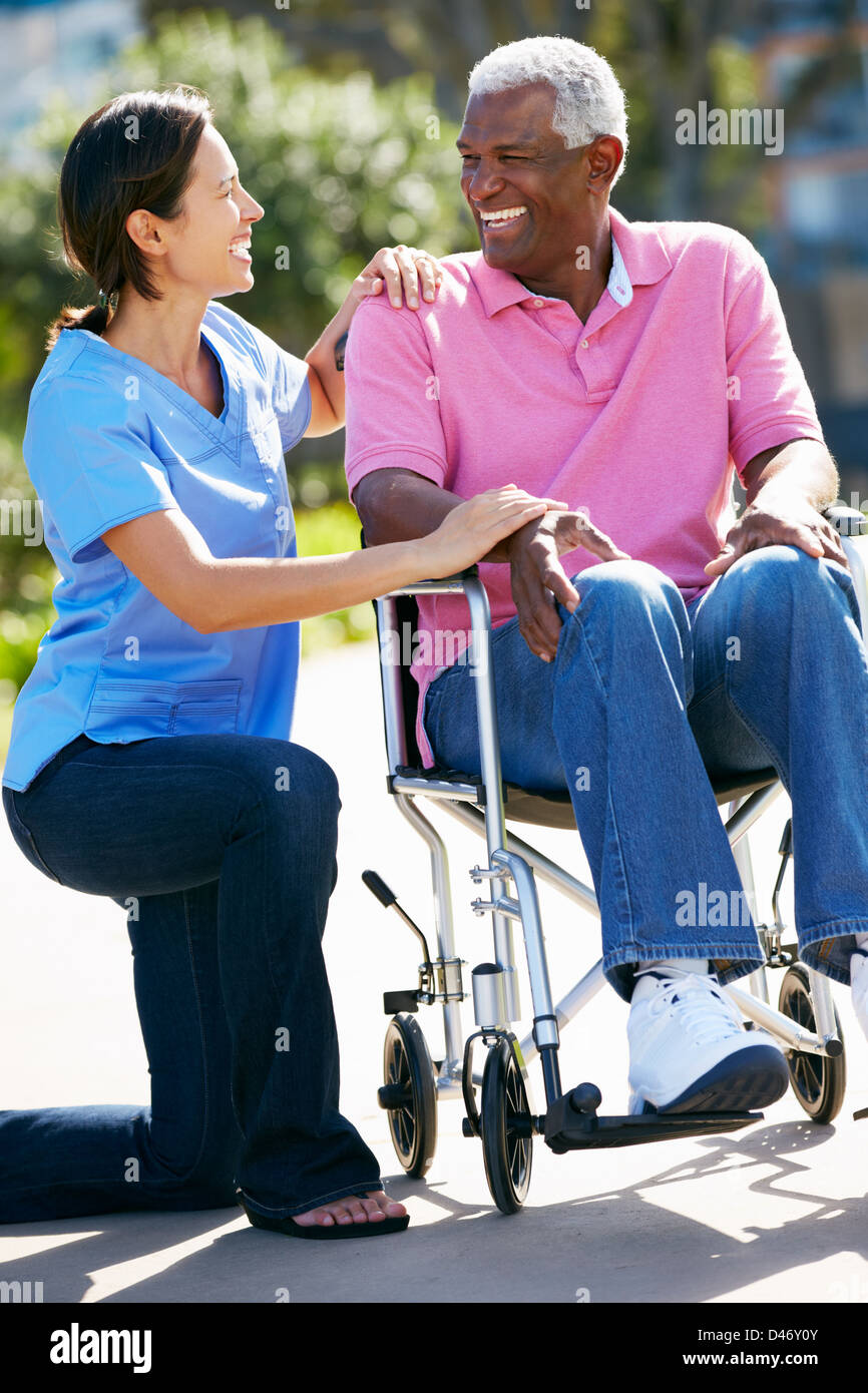 Carer Pushing Senior Man In Wheelchair Stock Photo