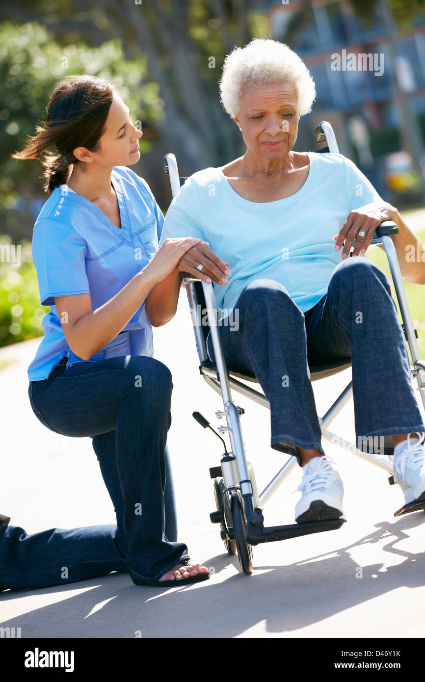 Carer Pushing Unhappy Senior Woman In Wheelchair Stock Photo