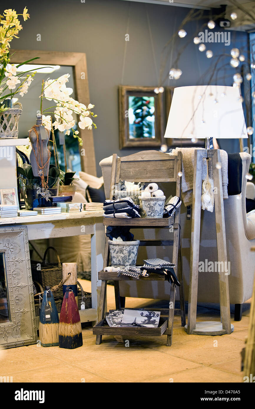 Image of shop display including white wash desk, wooden trestle, linen, candles, tall lamp, large mirror, arm chair, cane basket Stock Photo