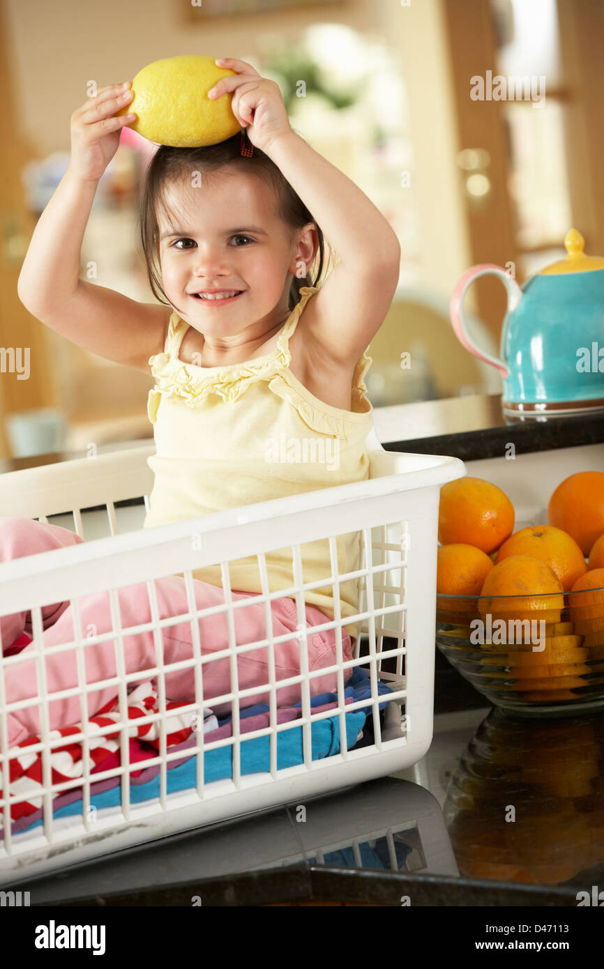 Girl Sitting In Laundry Basket On Kitchen Counter With Lemon Stock