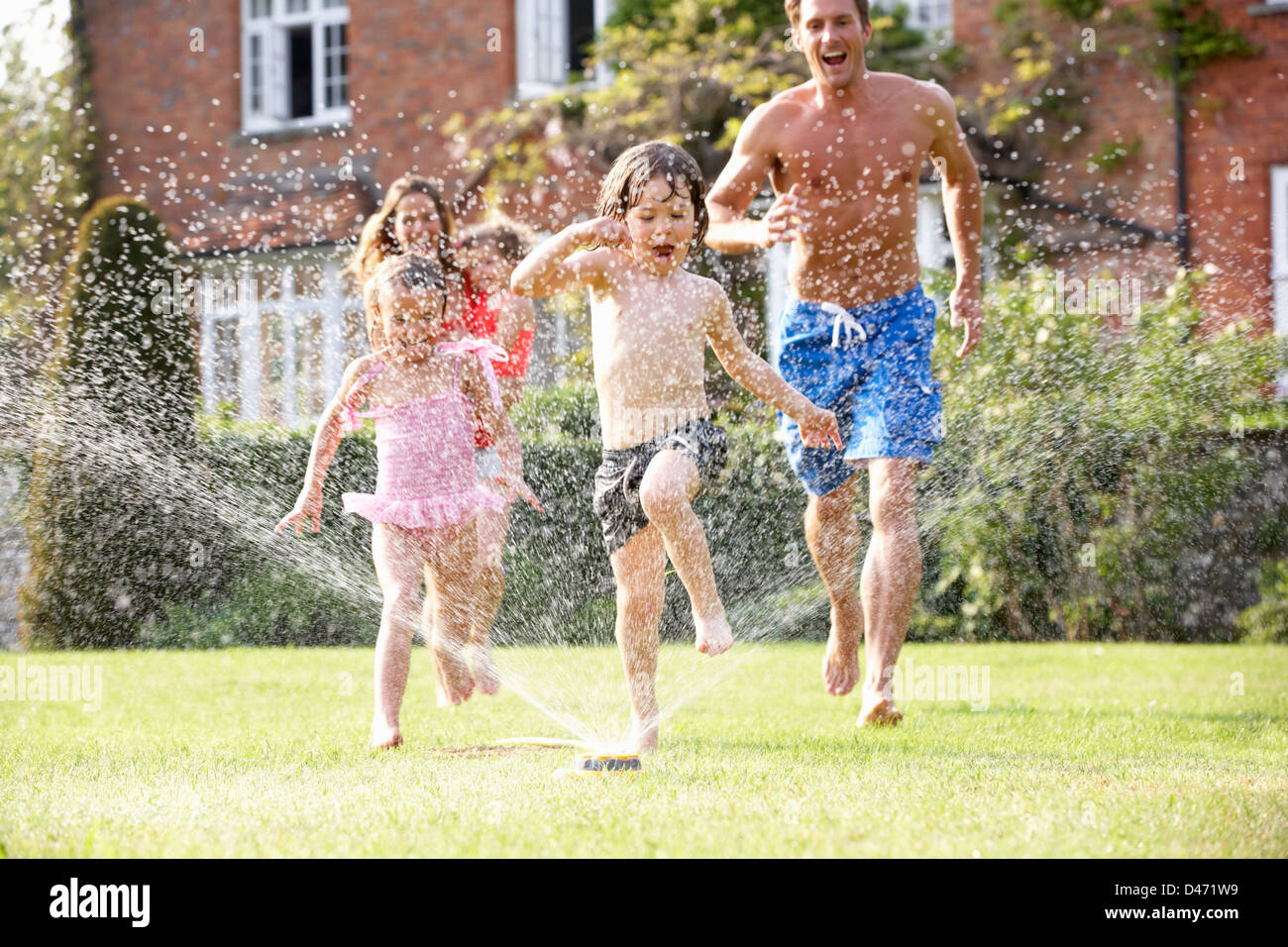 Family Running Through Garden Sprinkler Stock Photo Alamy