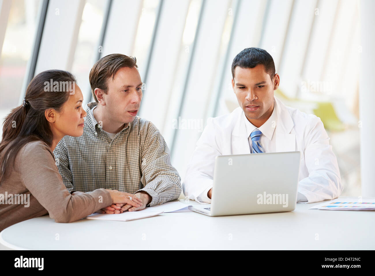 Doctor Using Laptop Discussing Treatment With Patients Stock Photo