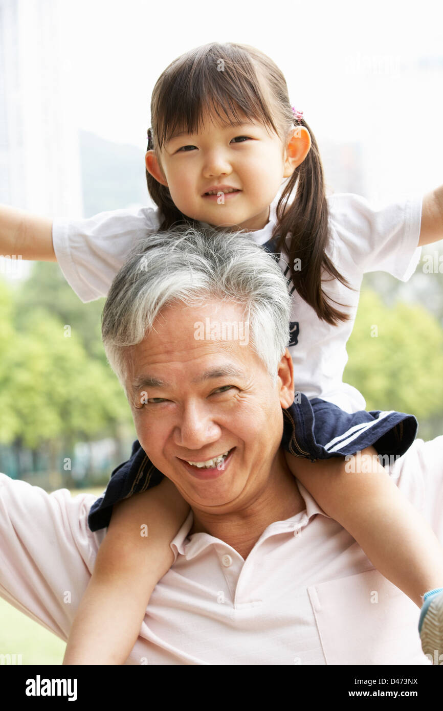 Chinese Grandfather Giving Granddaughter Ride On Shoulders In Park Stock Photo