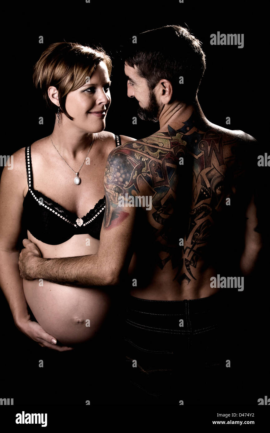 Image of couple in love cuddling man has his arm around her large pregnant belly Stock Photo