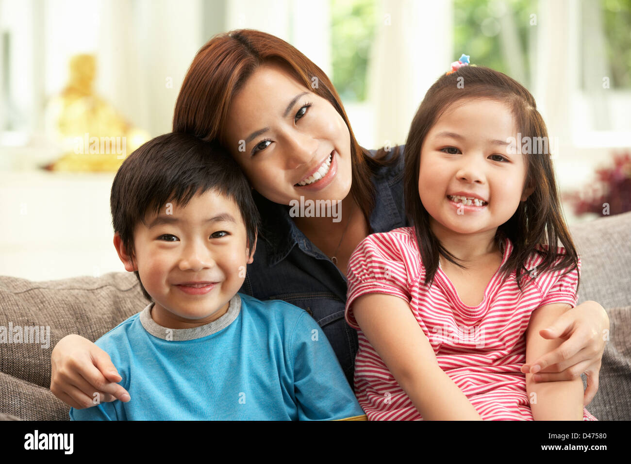 Chinese Mother And Children Sitting On Sofa At Home Together Stock Photo