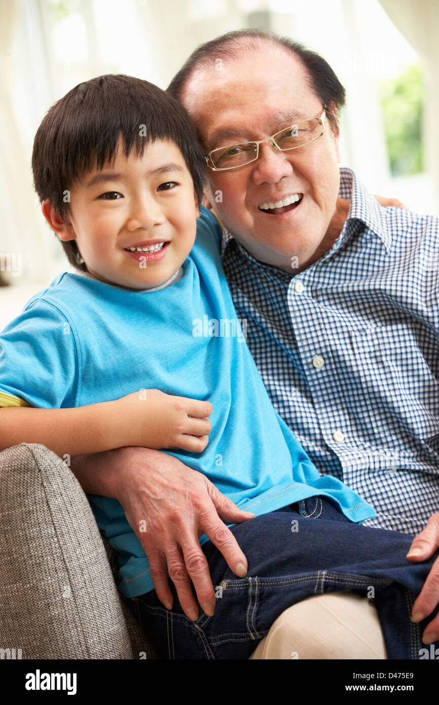 Chinese Grandfather And Grandson Relaxing On Sofa At Home Stock Photo