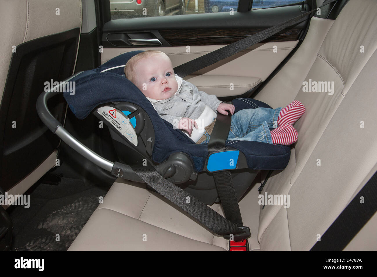 Baby boy sixth months old sitting in a car seat secured with a seatbelt. Stock Photo