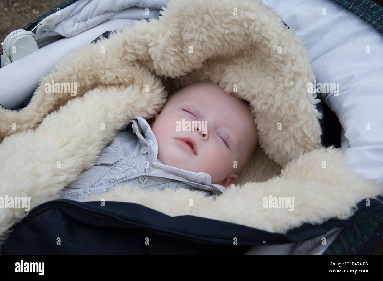 Six month old baby boy sleeping in his pram with a warm lambswool blanket Stock Photo
