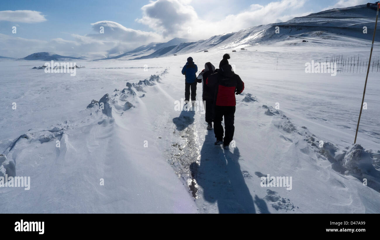 Three people trying to walk on road that has been blown over with snow outside Longyearbyen in Spitsbergen Stock Photo