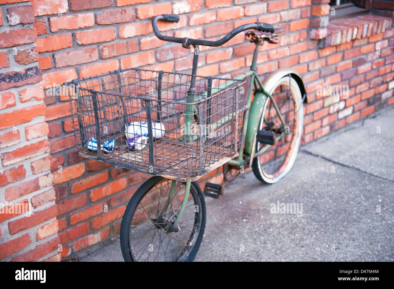 A vintage bicycle against a red brick wall with trash in basket Stock Photo