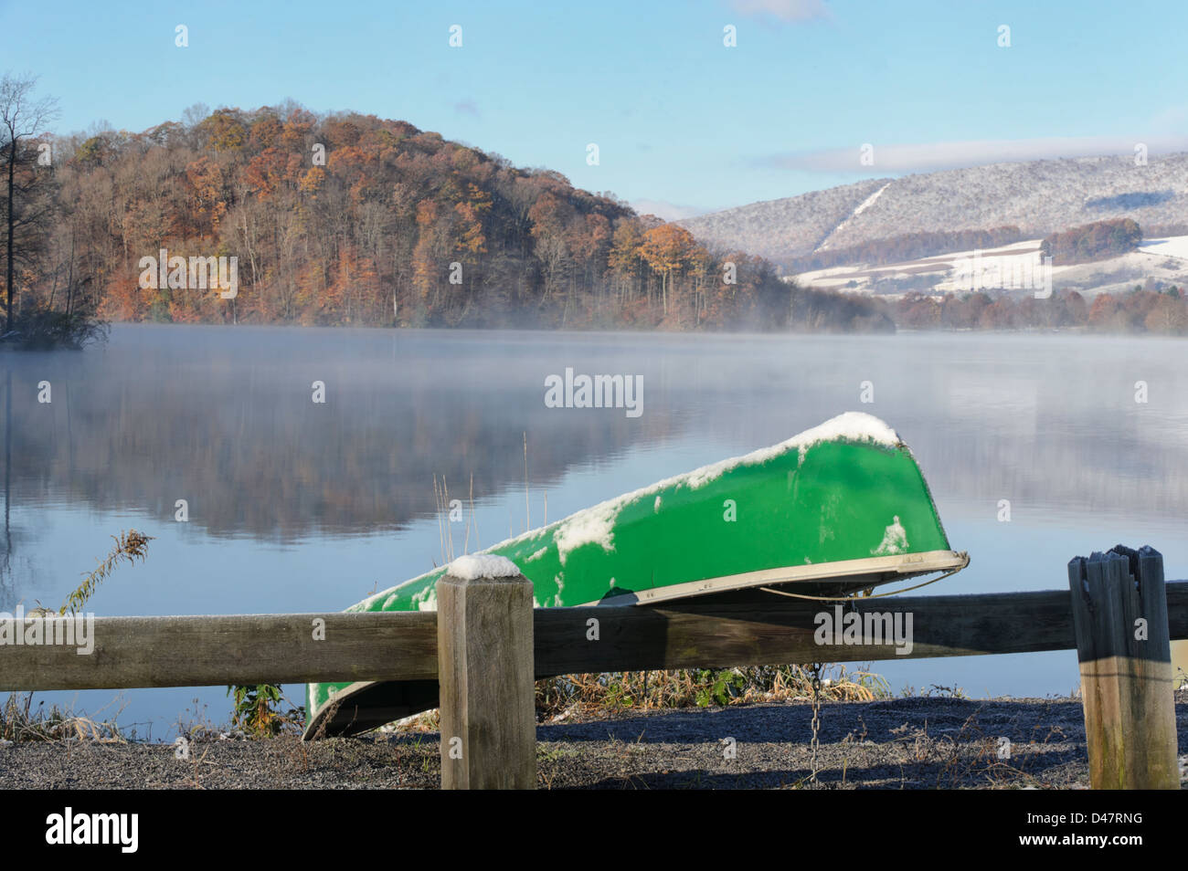 Canoe at a snowy a foggy lake in cold morning sunshine, fall mountain
