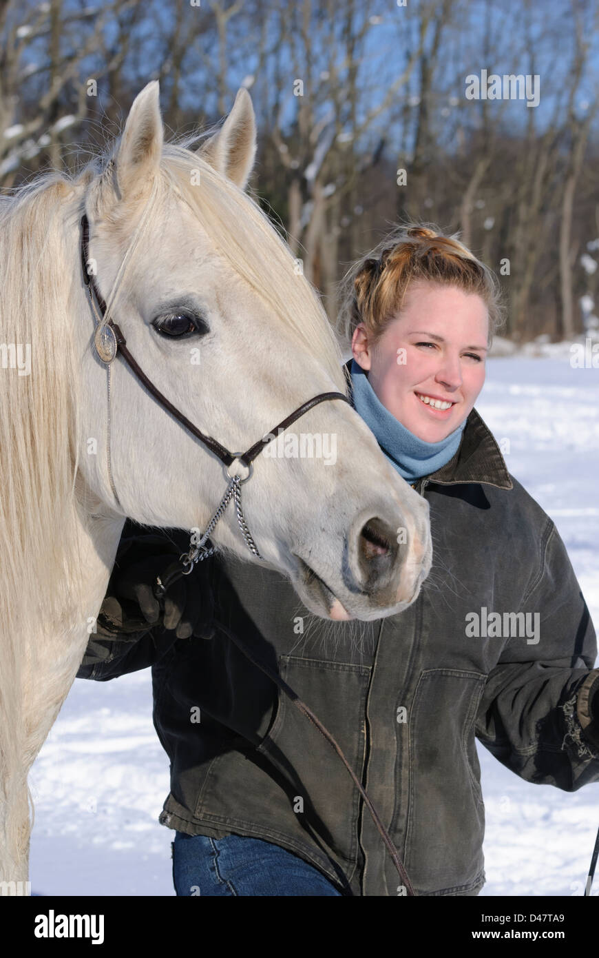 Woman and her white horse in outdoor winter snow portrait, a twenty-something blond and an Arabian stallion. Stock Photo