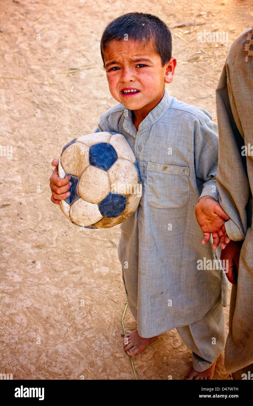 Kandahar, Afghanistan - May 22, 2010:  An Afghan boy with a deflated soccer ball asks passing Soldiers for a pen. Stock Photo