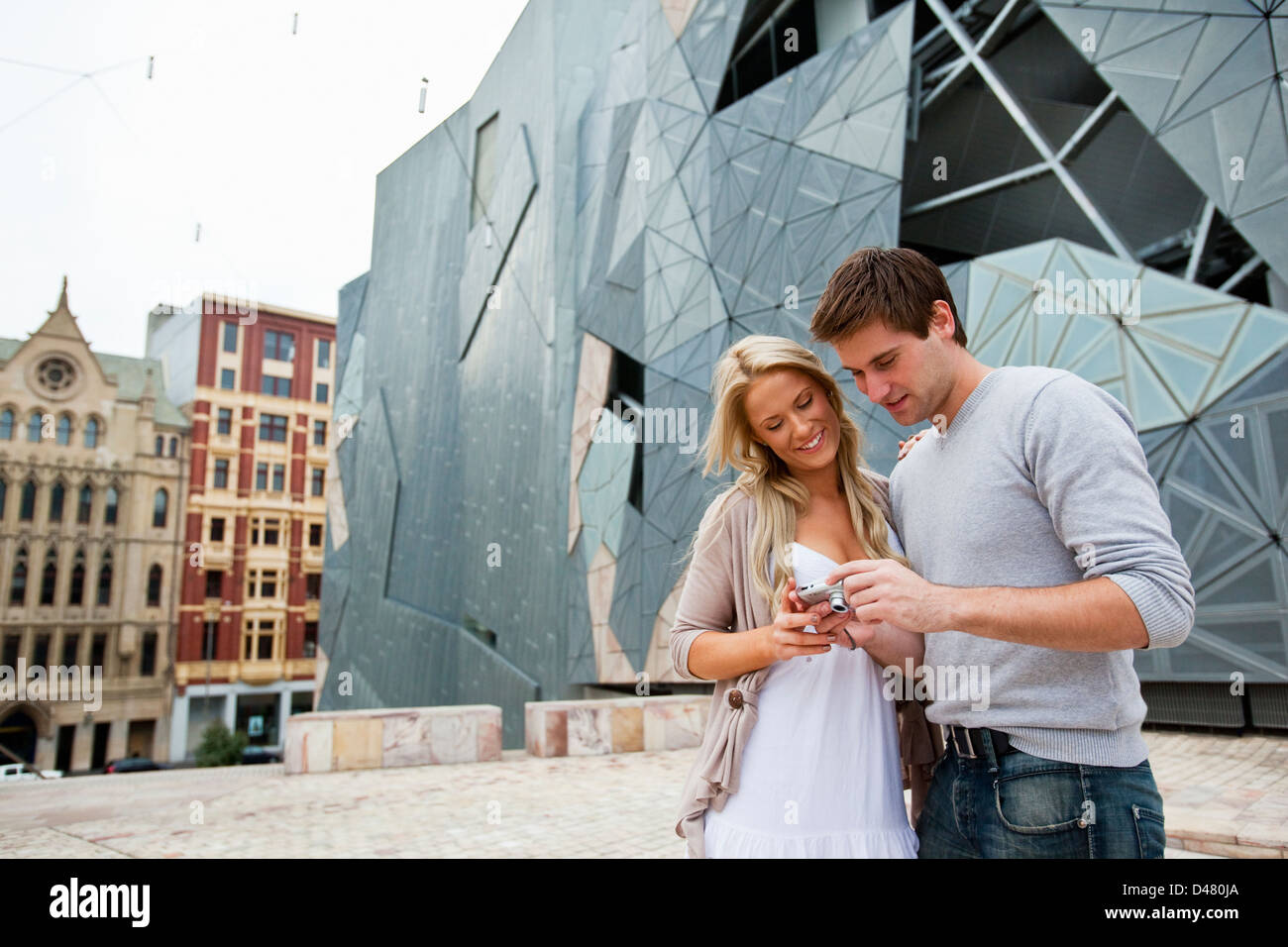 Young couple sightseeing in city, looking at photos on camera. Federation Square, Melbourne, Victoria, Australia Stock Photo
