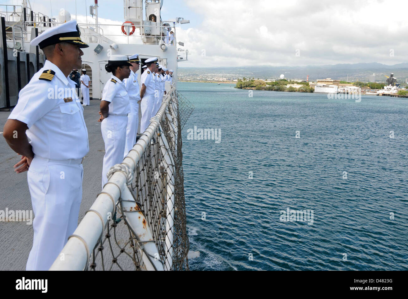 Sailors aboard a U.S. Navy vessel stand at attention on the rails, a ...