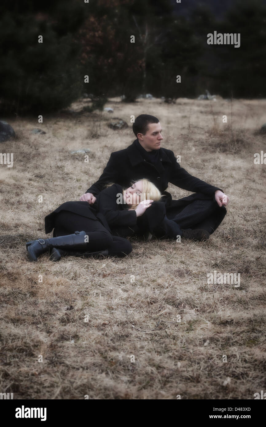 a couple in black clothes is lying on a meadow in winter Stock Photo